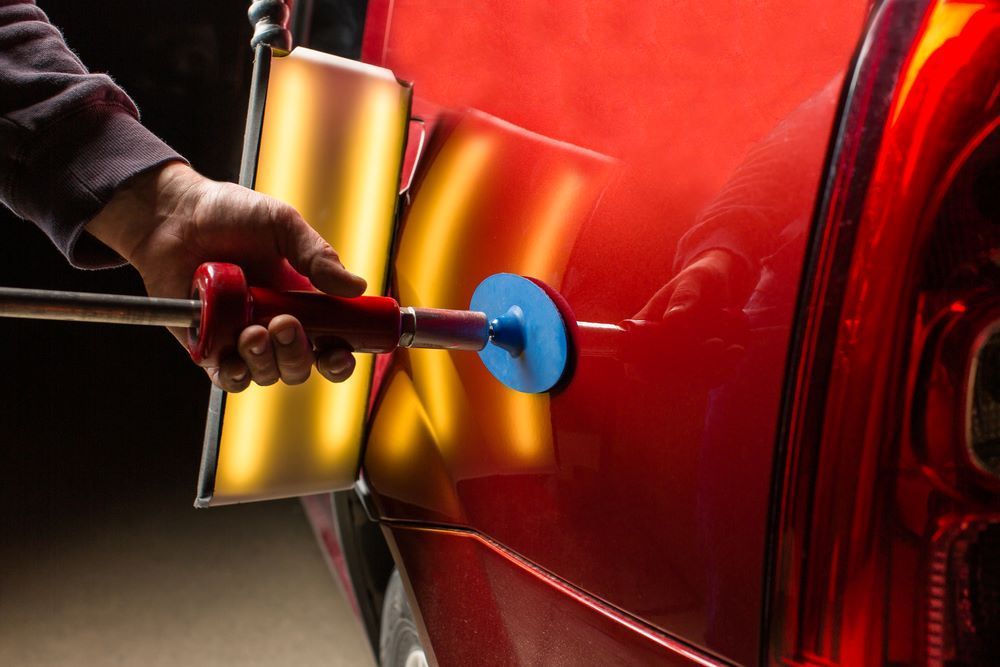 A Person is Using a Tool to Fix a Dent on a Red Car — Smash Repairs In Taree, NSW