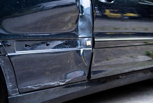A Black Car With a Damaged Side Door is Parked on the Side of the Road — Smash Repairs In Old Bar, NSW