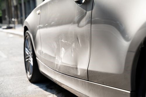 A Silver Car With a Damaged Door is Parked on the Side of the Road — Smash Repairs In Wingham, NSW