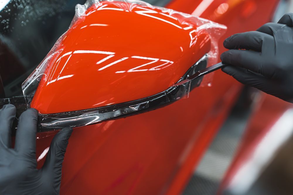 A Person is Wrapping a Red Car With Plastic Wrap — Smash Repairs In Taree, NSW