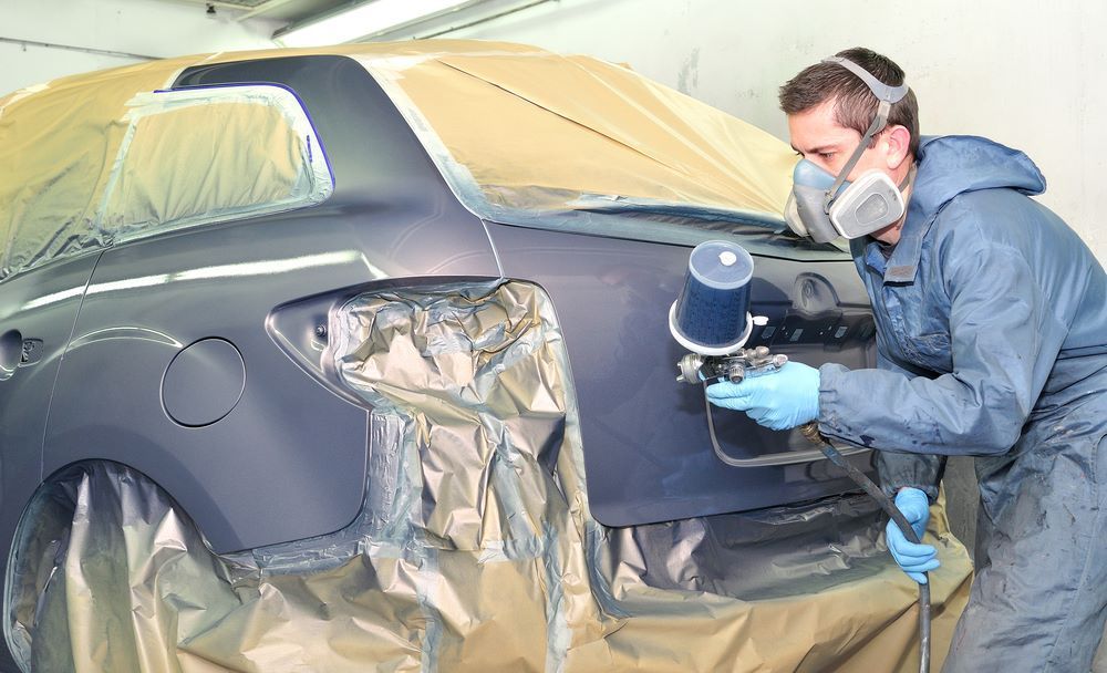 A Man Wearing a Mask is Spray Painting a Car — Smash Repairs In Tuncurry, NSW