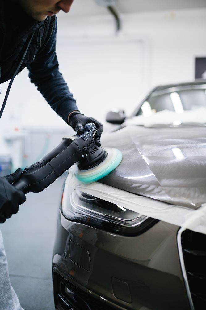 A Man is Polishing a Car With a Machine in a Garage — Smash Repairs In Hallidays Point, NSW