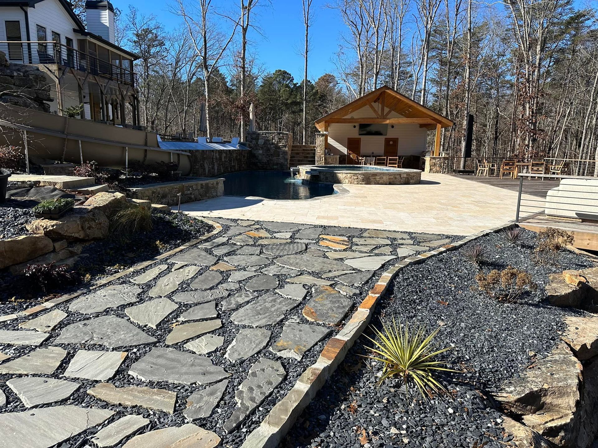 Stone pathway leads to outdoor living space with a covered structure, pool, and surrounding landscaping.