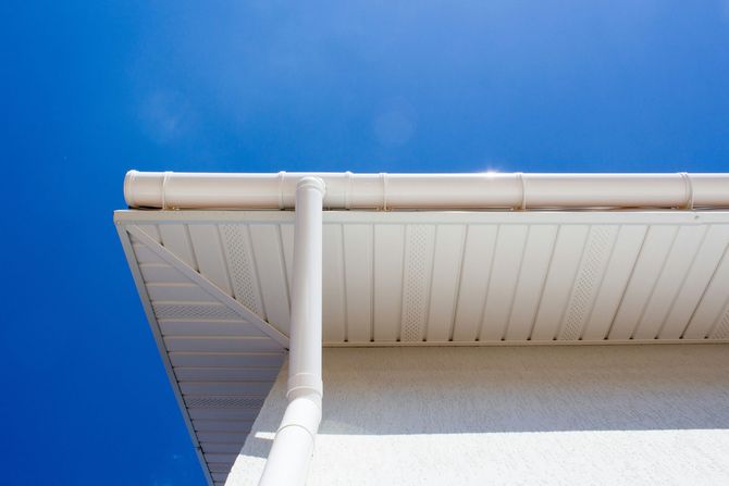 A white house gutter and downspout against a clear blue sky.