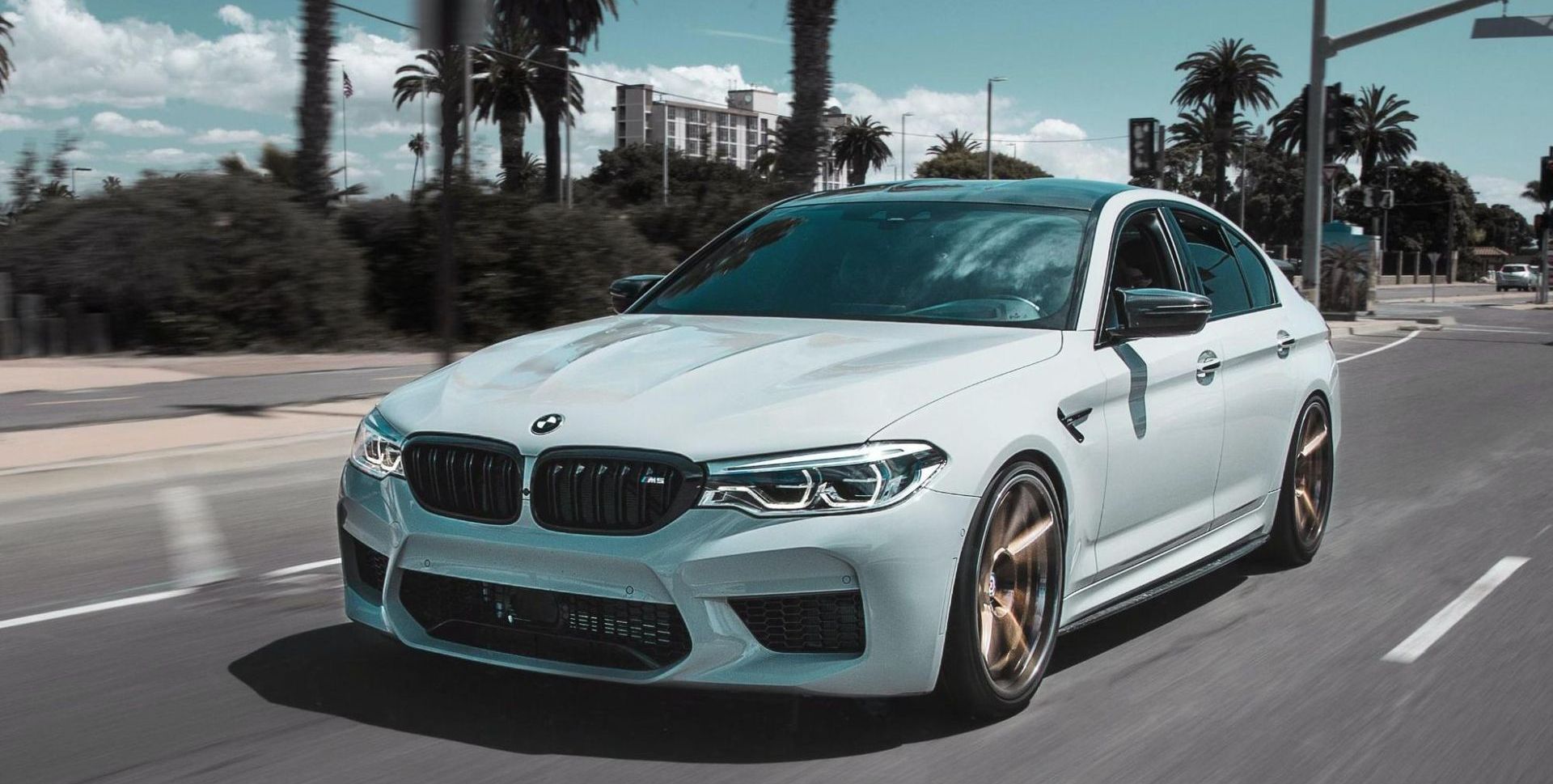 A white bmw m5 is driving down a city street.