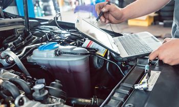 A man is working on a car engine with a laptop.