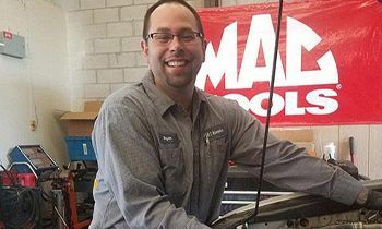 A man is working on a car in a garage in front of a mac tools sign.