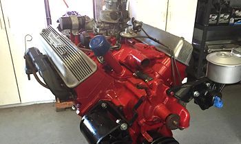 A red engine is sitting on top of a concrete floor in a garage.