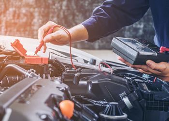 A mechanic is working on a car with a multimeter.