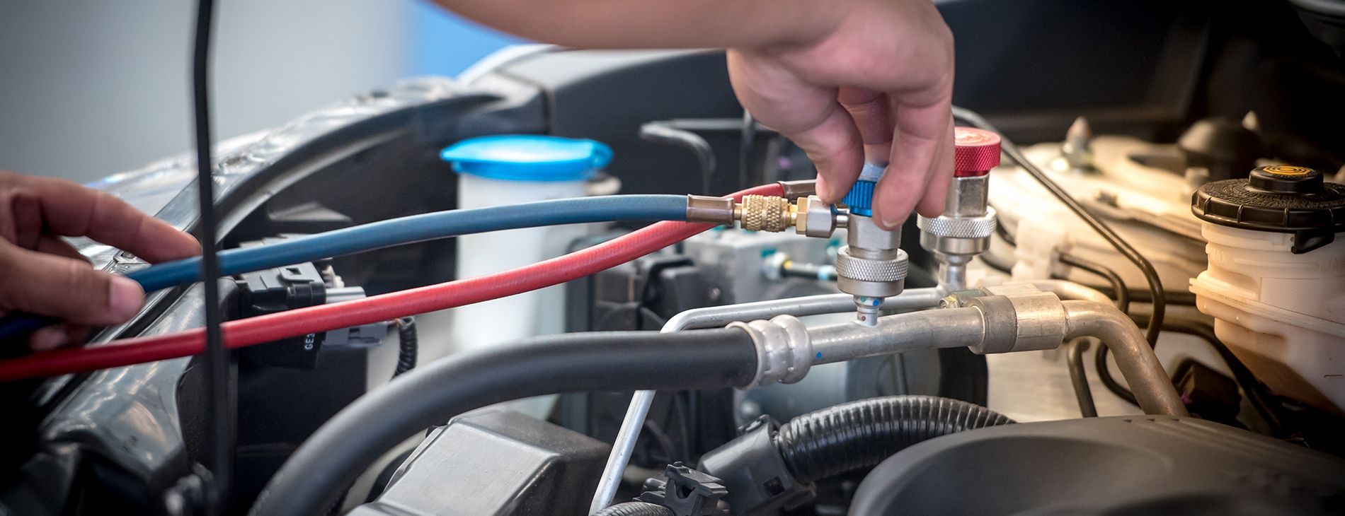 Hands adjusting car engine components with red and black hoses in a mechanical bay