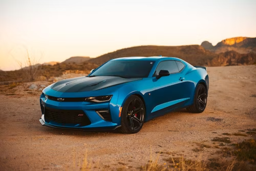 Blue Chevrolet Camaro sports car parked on a dirt road in front of mountains.