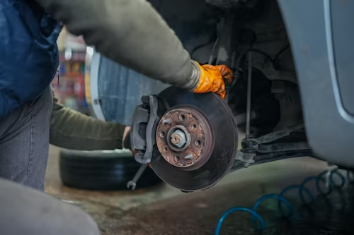 Mechanic holding a brake disc while working on a car wheel hub in a garage