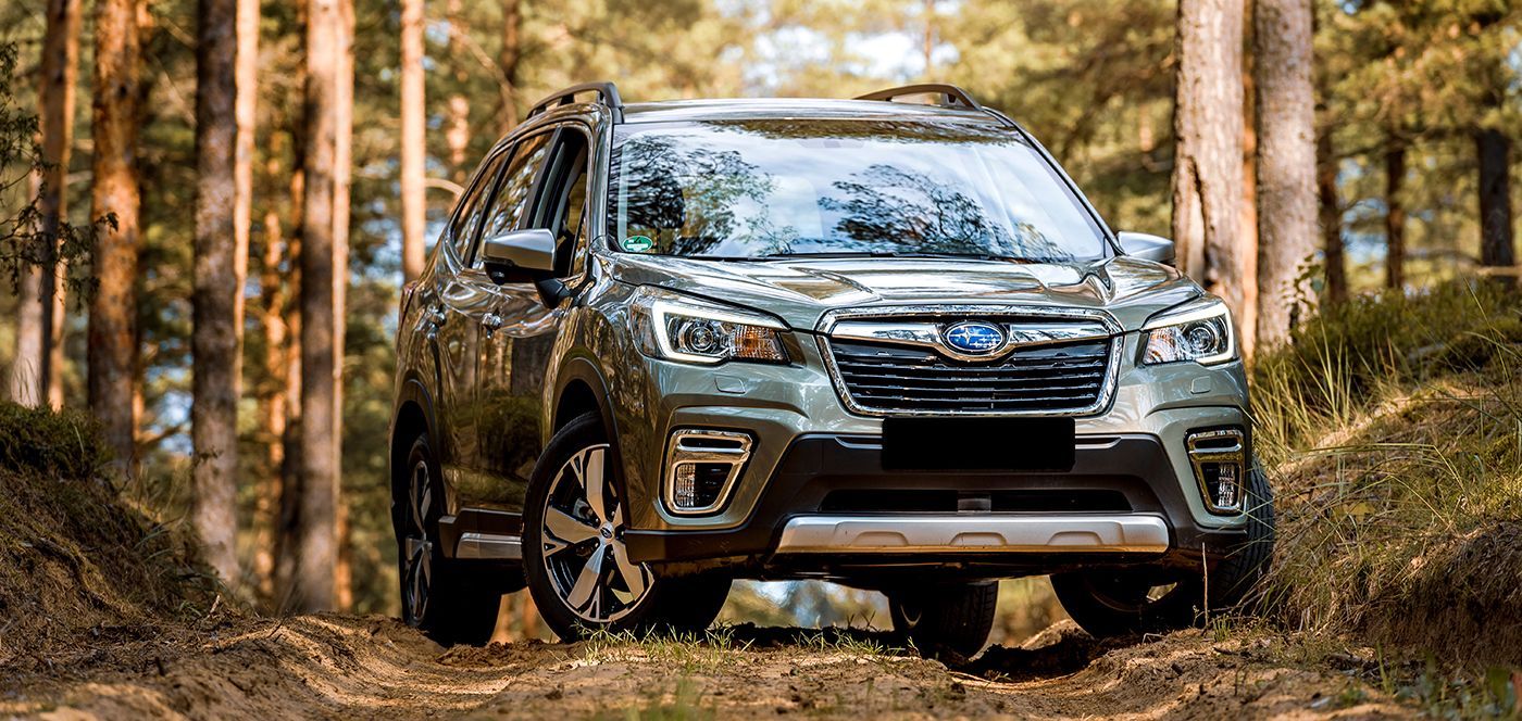 Dark green Subaru Forester SUV parked on a dirt path in a forest.