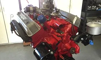 A freshly painted red V8 engine with silver finned valve covers, mounted on a stand inside a garage.