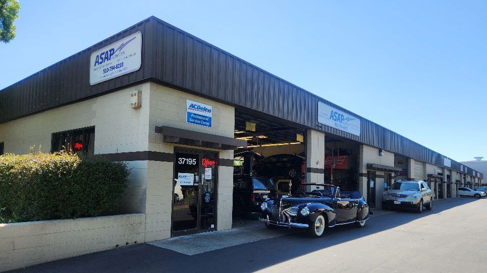 A black car is parked in front of a car repair shop.