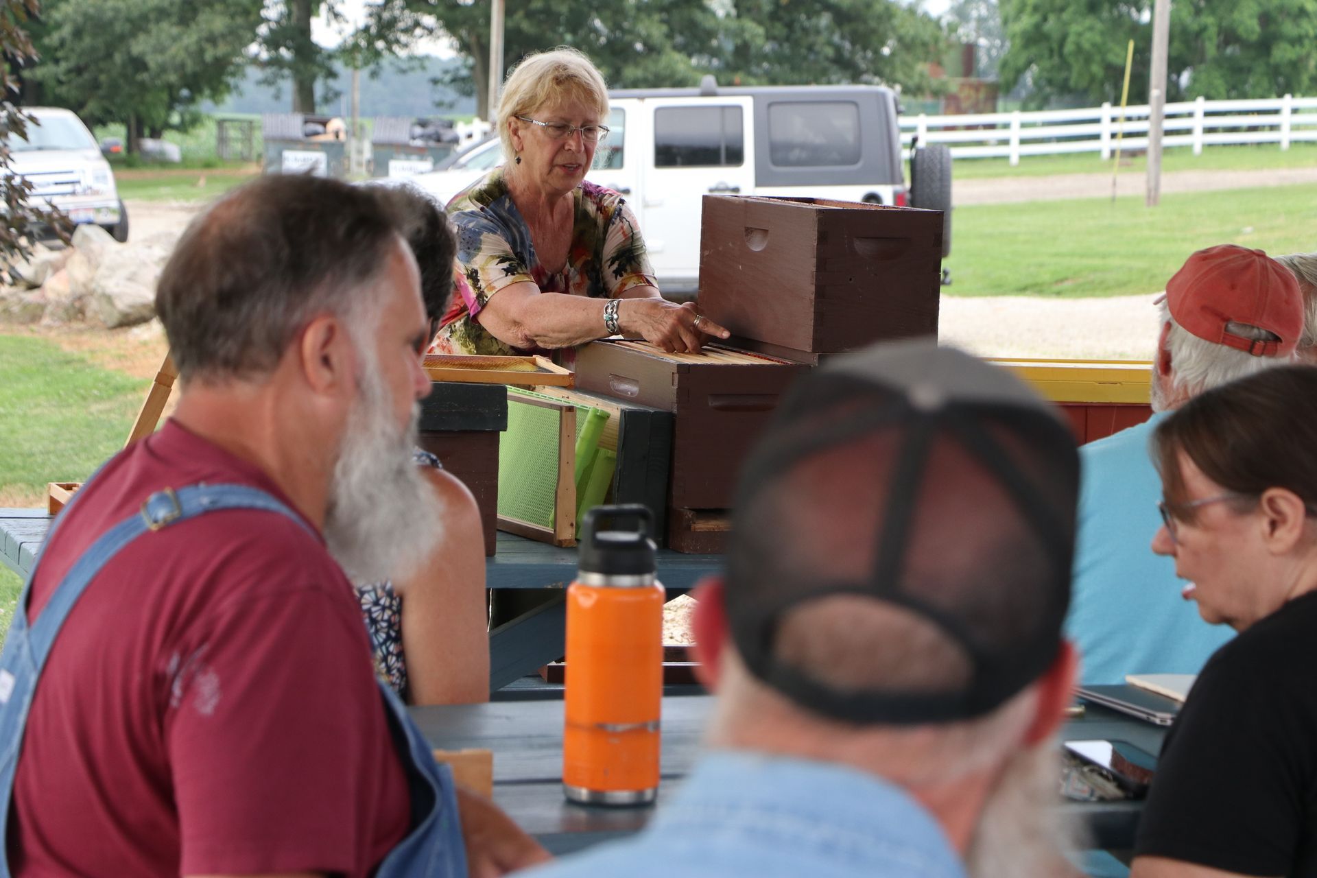 A group of people are sitting around a table looking at a beehive