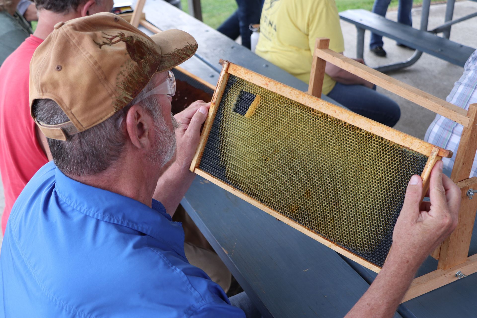 A man is sitting at a table holding a beehive frame.