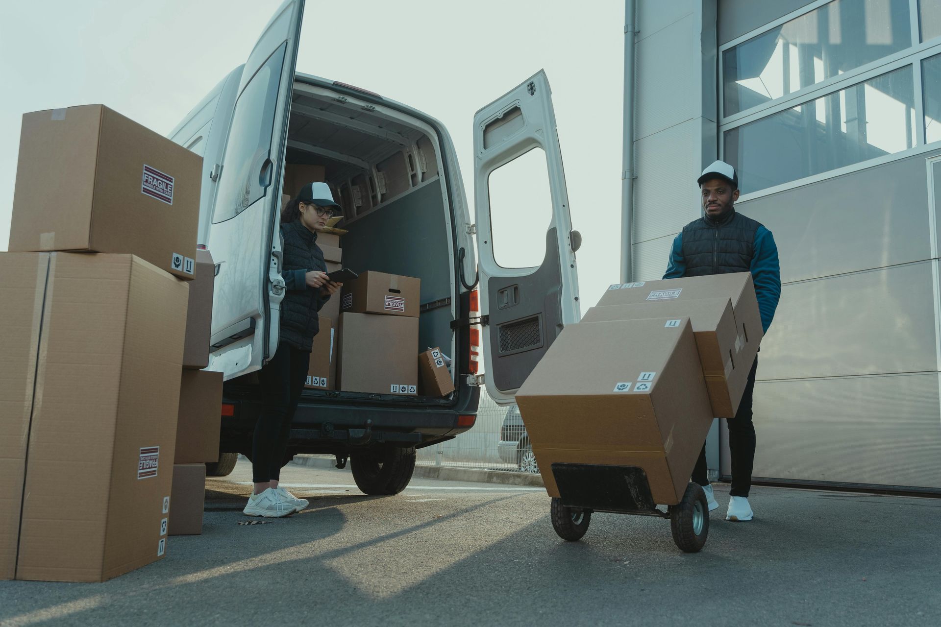 Deux personnes chargent des cartons dans une camionnette, l'une d'elles utilisant un diable.