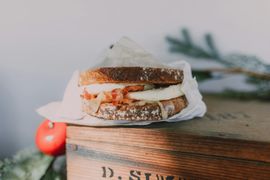 Un sandwich au fromage grillé emballé dans du papier, posé sur une boîte en bois avec une pomme rouge et de la verdure à proximité.