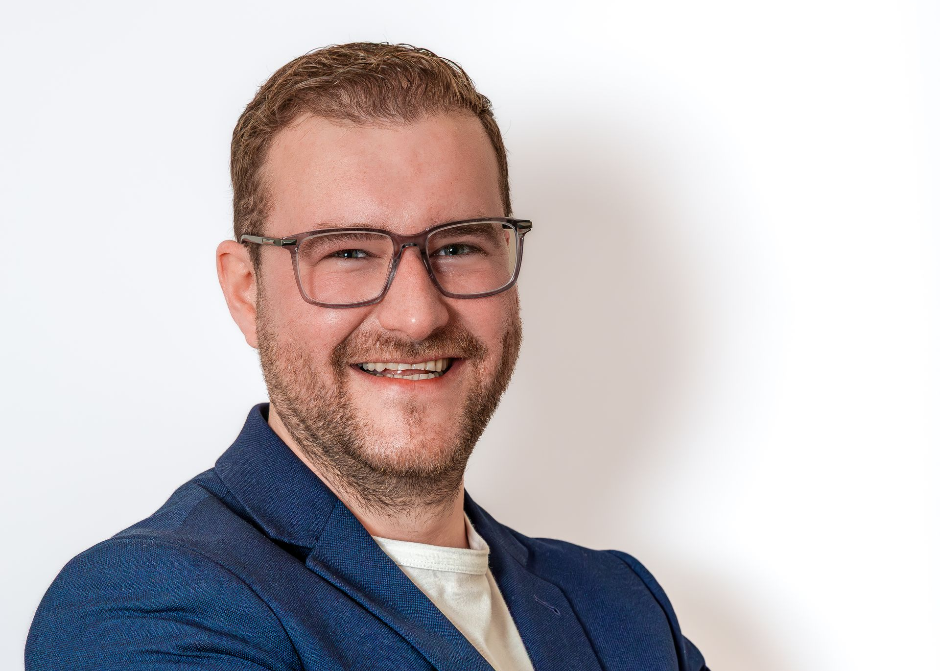 Homme souriant portant des lunettes et une veste bleue sur fond blanc