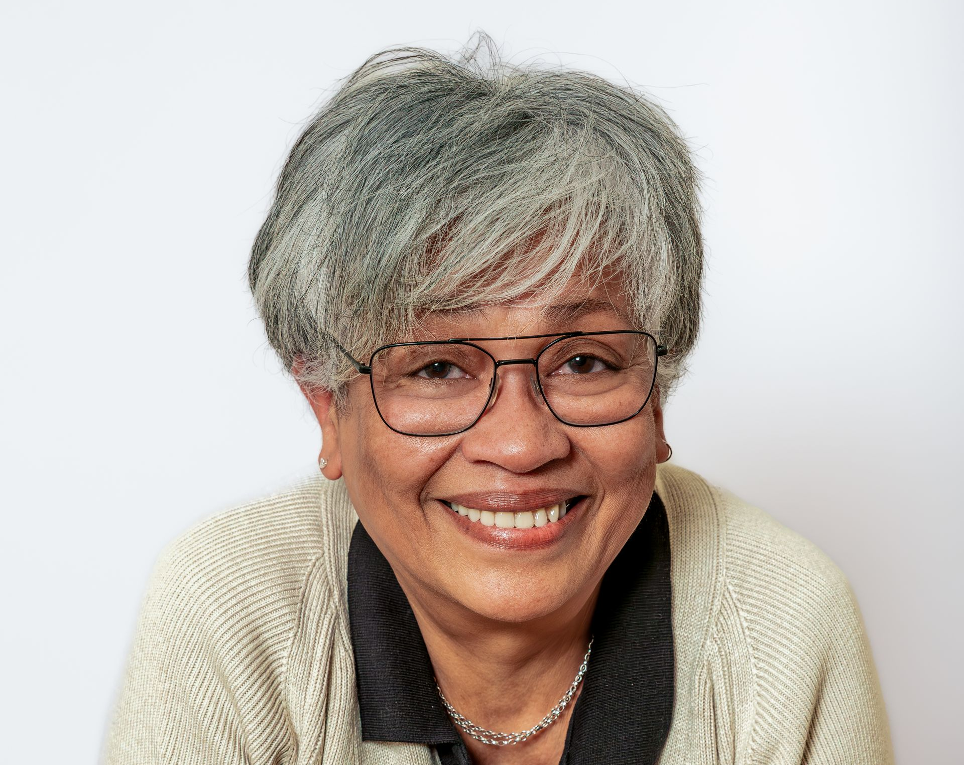 Personne souriante aux cheveux gris courts et portant des lunettes, vêtue d'un cardigan crème sur fond blanc