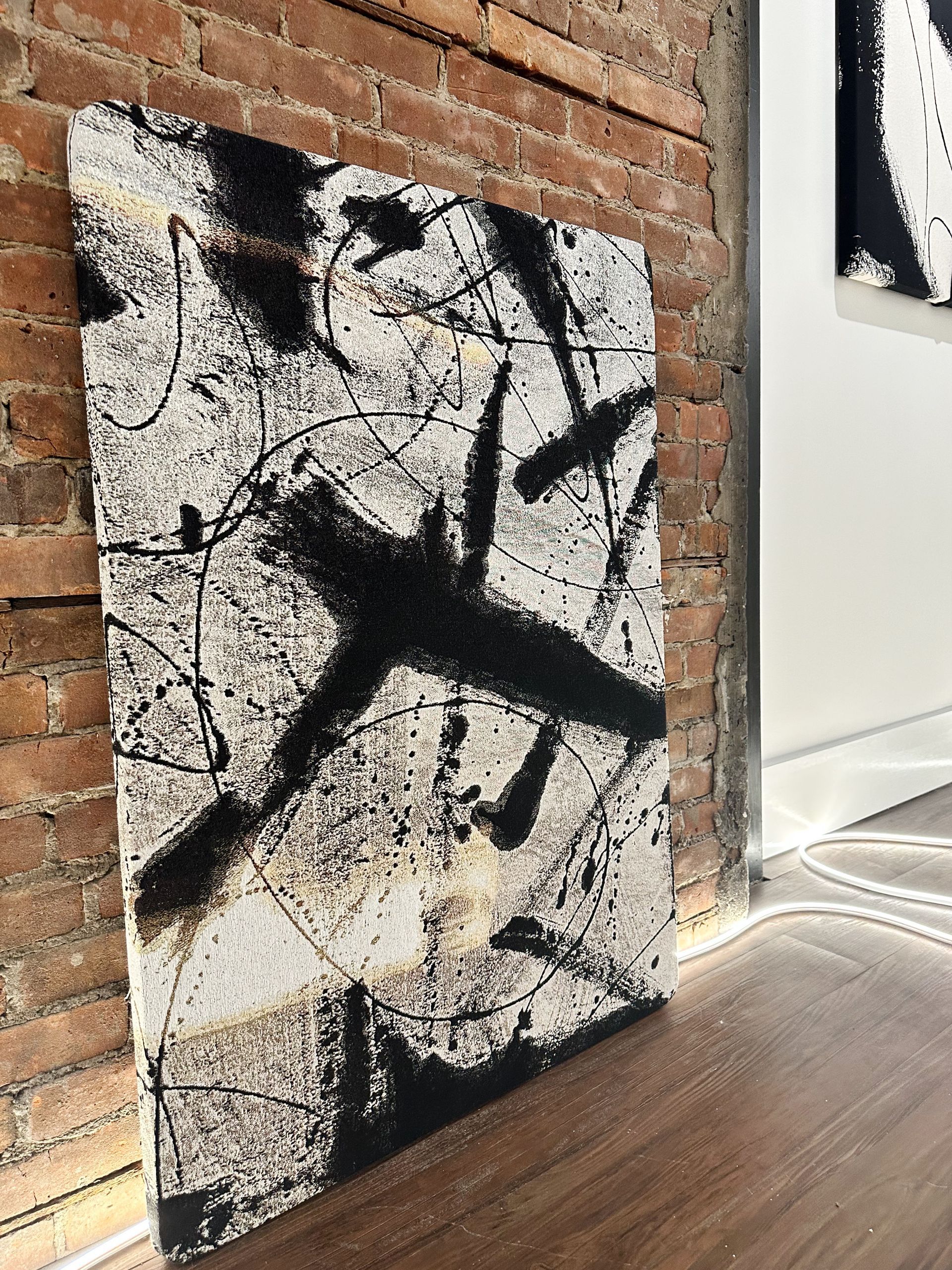A black and white painting is hanging on a brick wall.