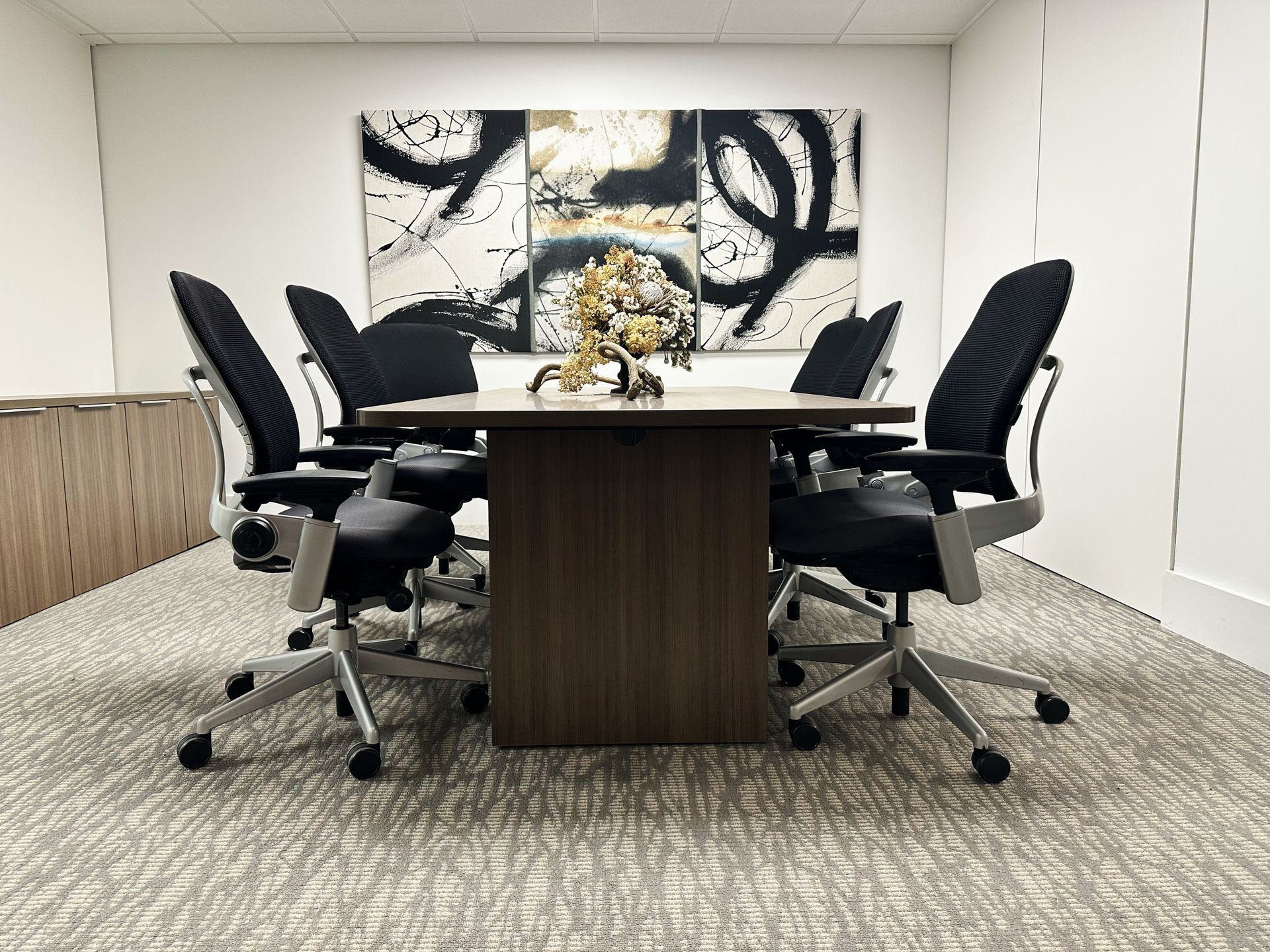 A conference room with a table and chairs and a painting on the wall.