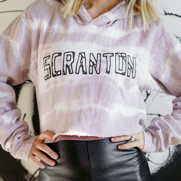 A woman is wearing a purple tie dye hoodie that says scranton