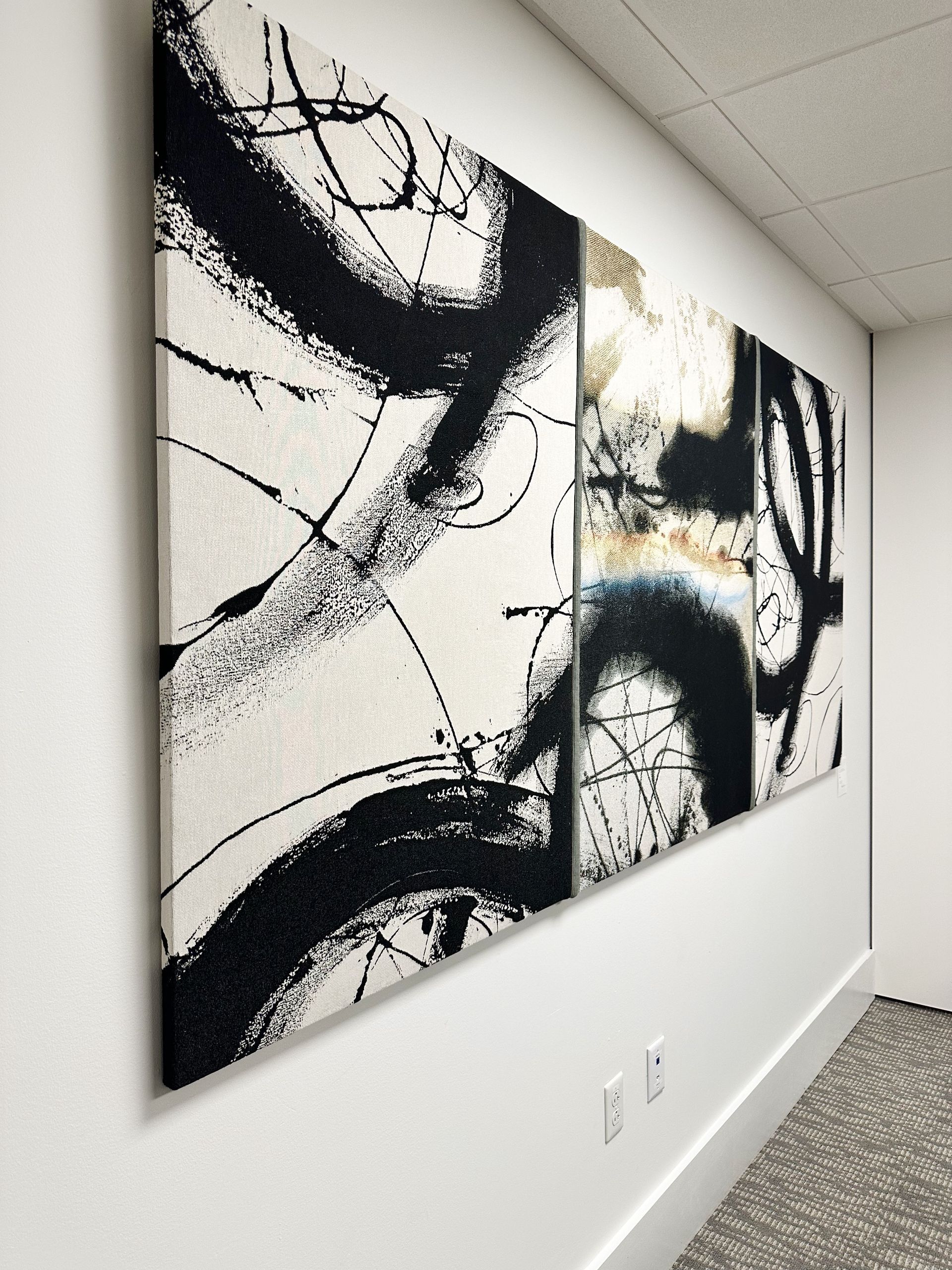 A large black and white painting hangs on a white wall