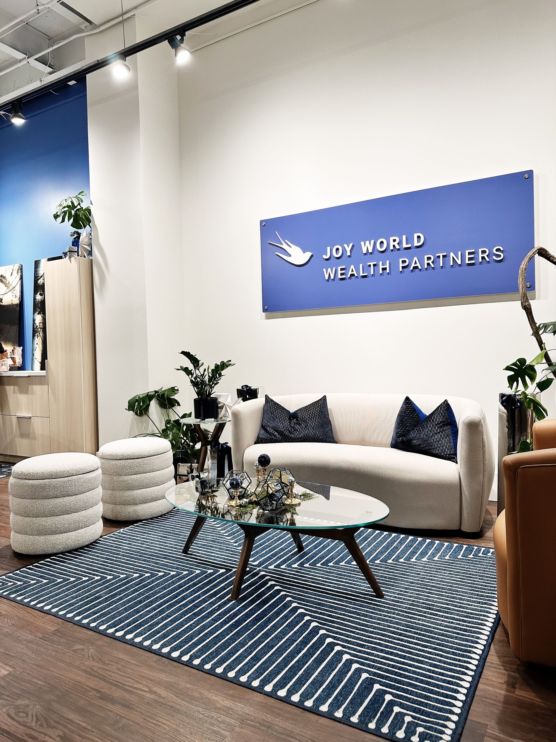 A living room with a couch , table , chairs and a sign that says joy world wealth partners.