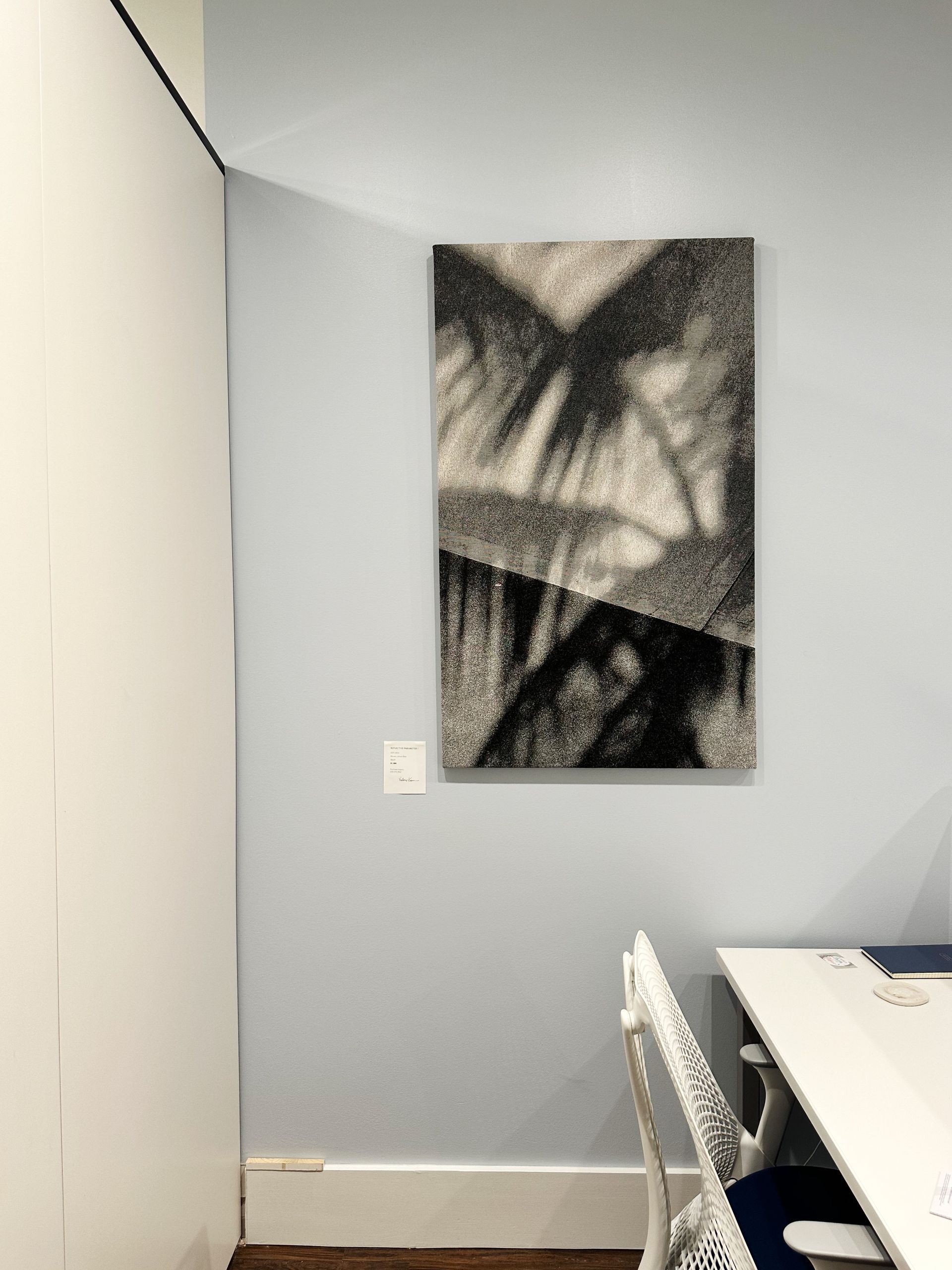 A painting is hanging on a wall above a desk in a room.