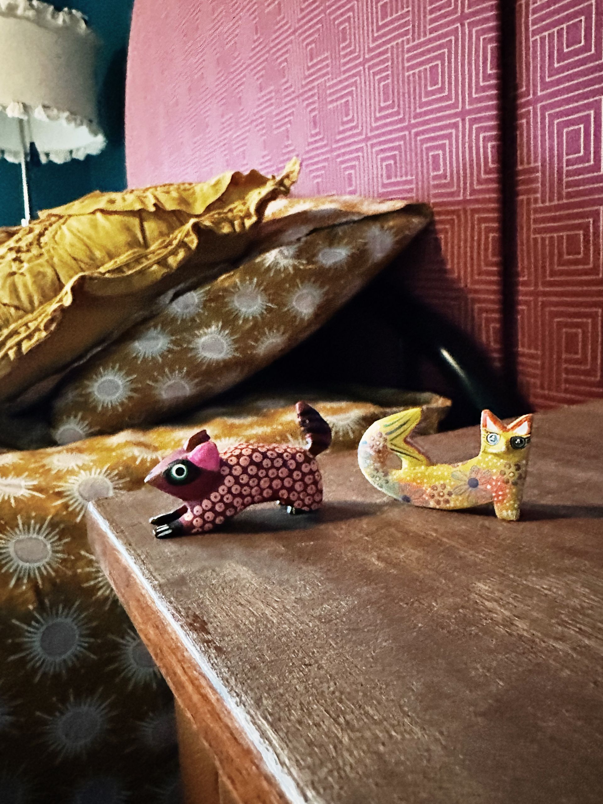 Two wooden animals are sitting on a wooden table next to a bed.