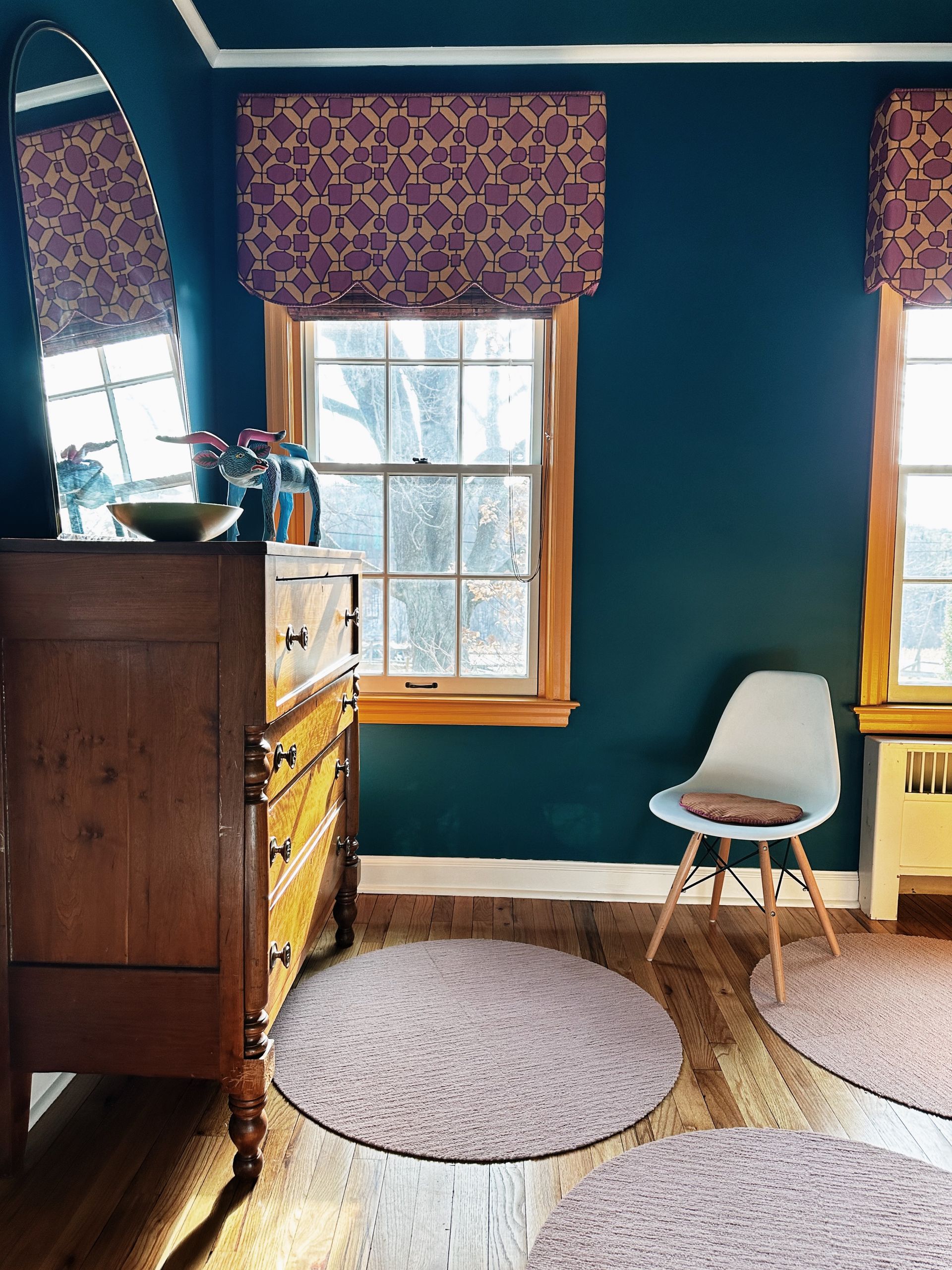A bedroom with blue walls , a dresser , a chair , and a mirror.