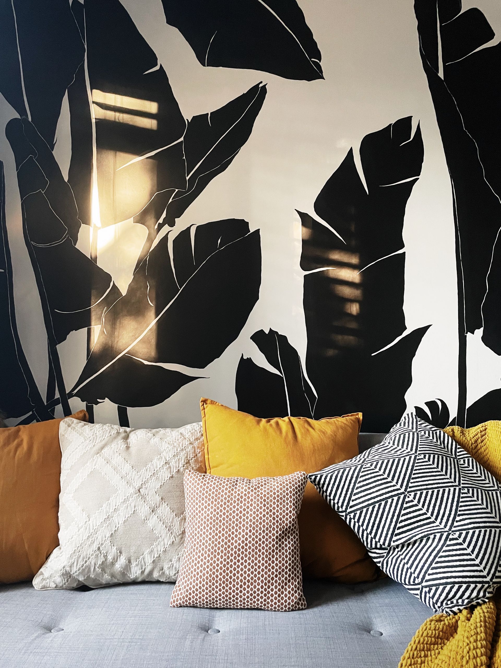 A couch with pillows in front of a wall with leaves on it
