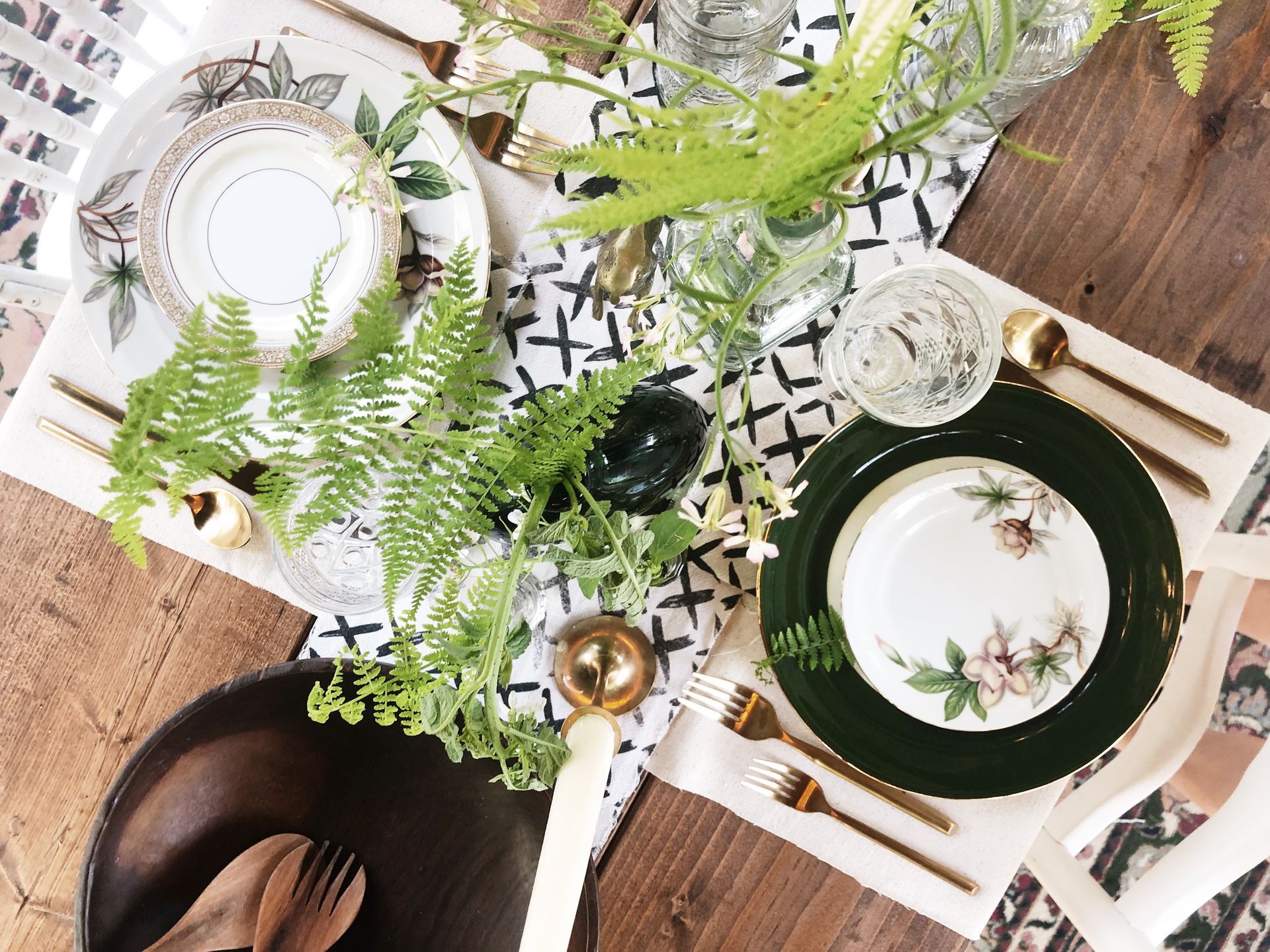 A table with plates , silverware , and ferns on it.