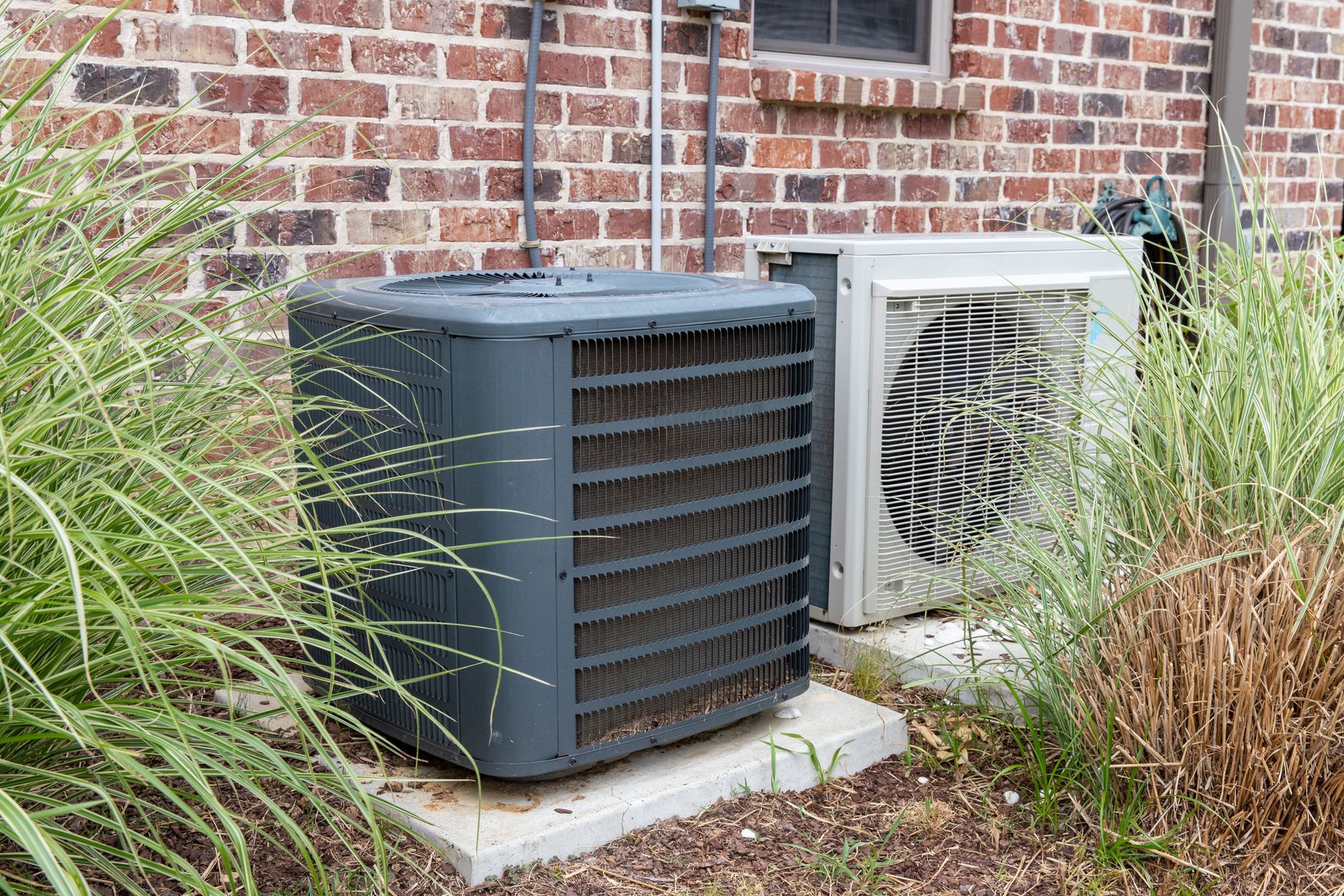 Two air conditioners are sitting outside of a brick building.