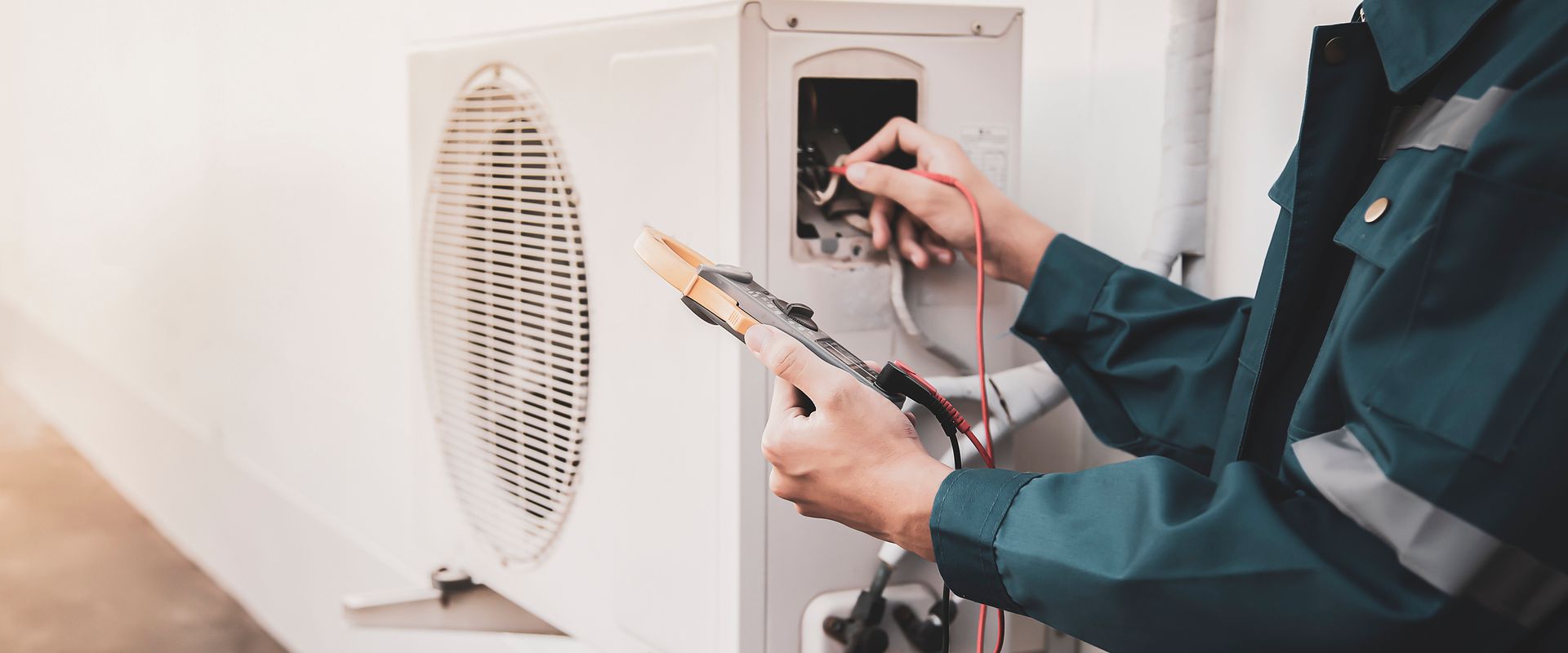 A man is working on an air conditioner while holding a clipboard.