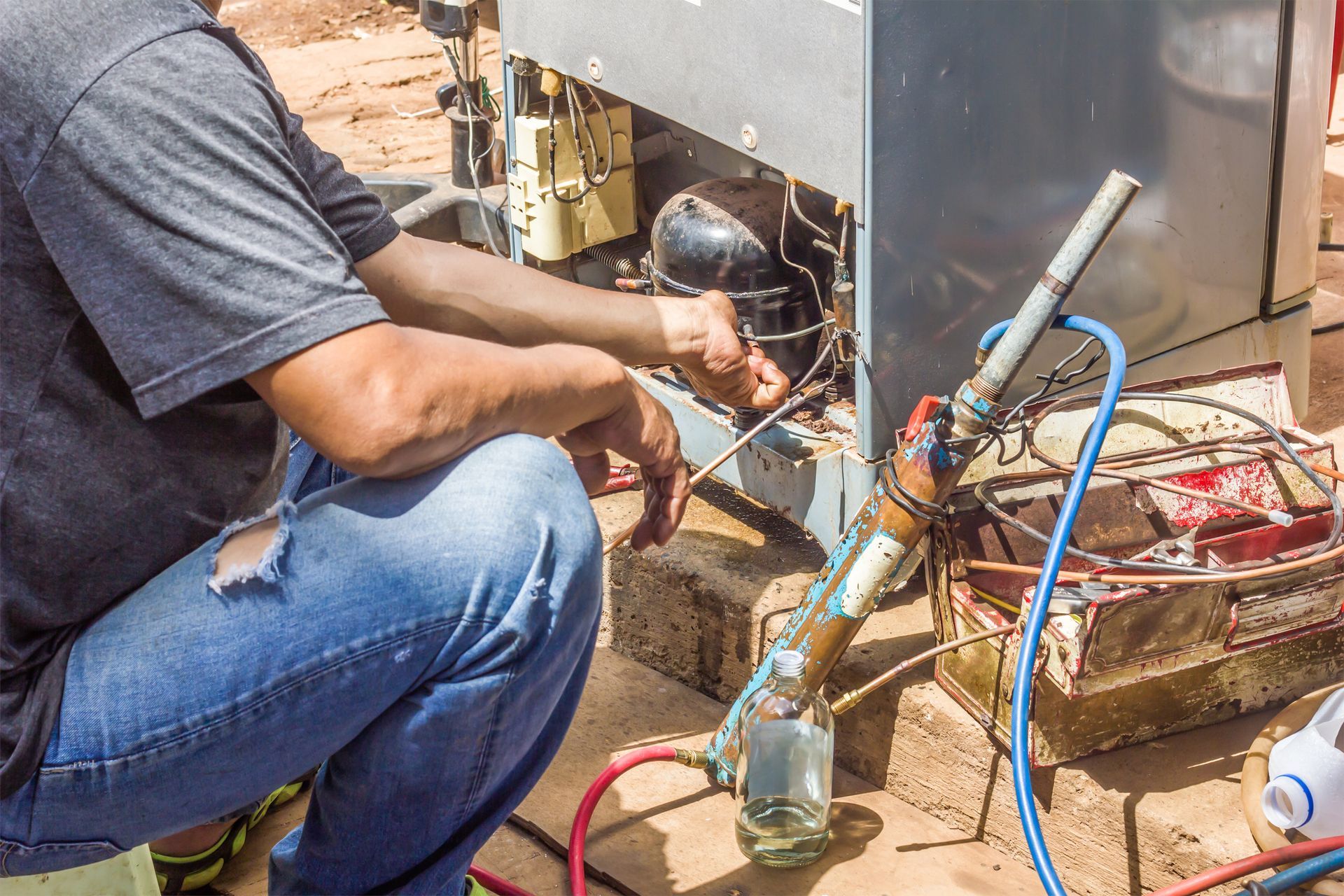 A man is kneeling down working on a refrigerator.