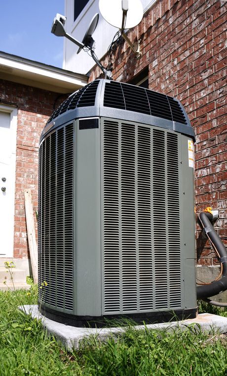A large air conditioner is sitting outside of a brick house.