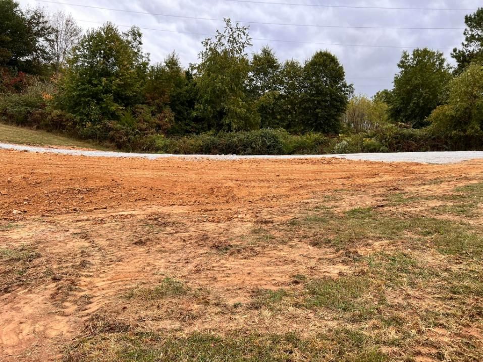 Dirt clearing with a road and trees under an overcast sky.