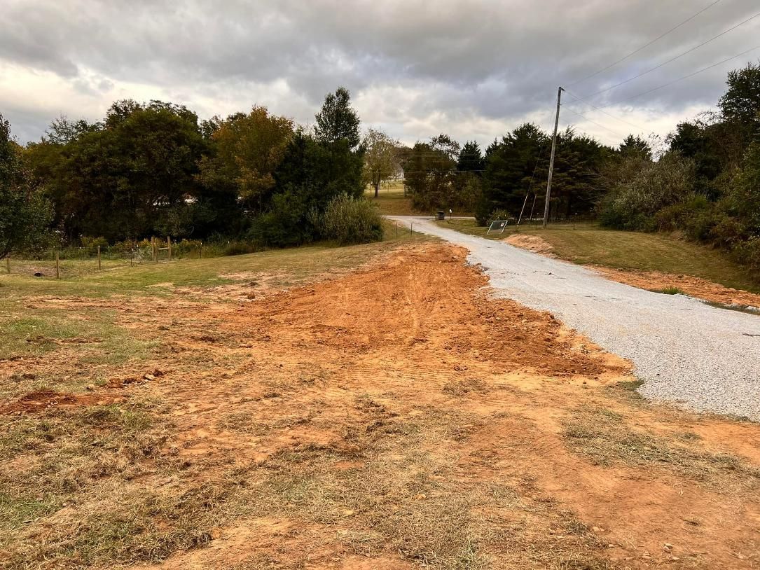 Dirt pile and gravel road leading toward trees under cloudy sky.