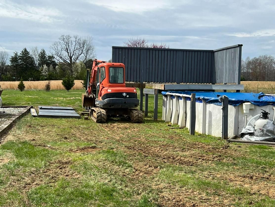 Orange excavator on muddy ground near a pool and container structure in a grassy field.