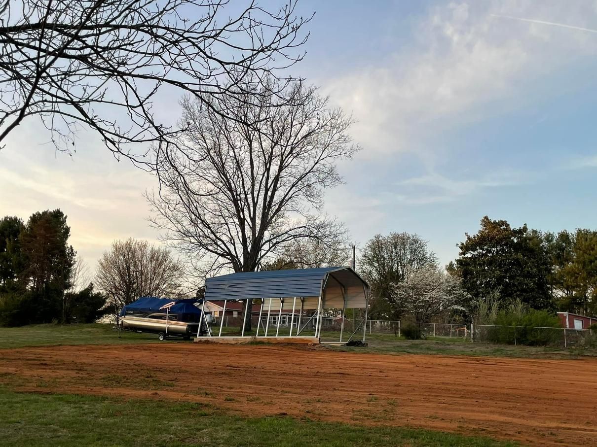 A small wooden building and a truck on a dirt lot with trees and a cloudy sky.