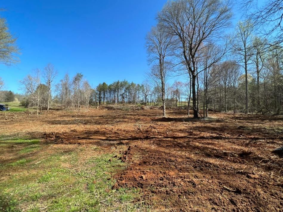 A cleared field of brown earth with trees and a forest in the background under a blue sky.
