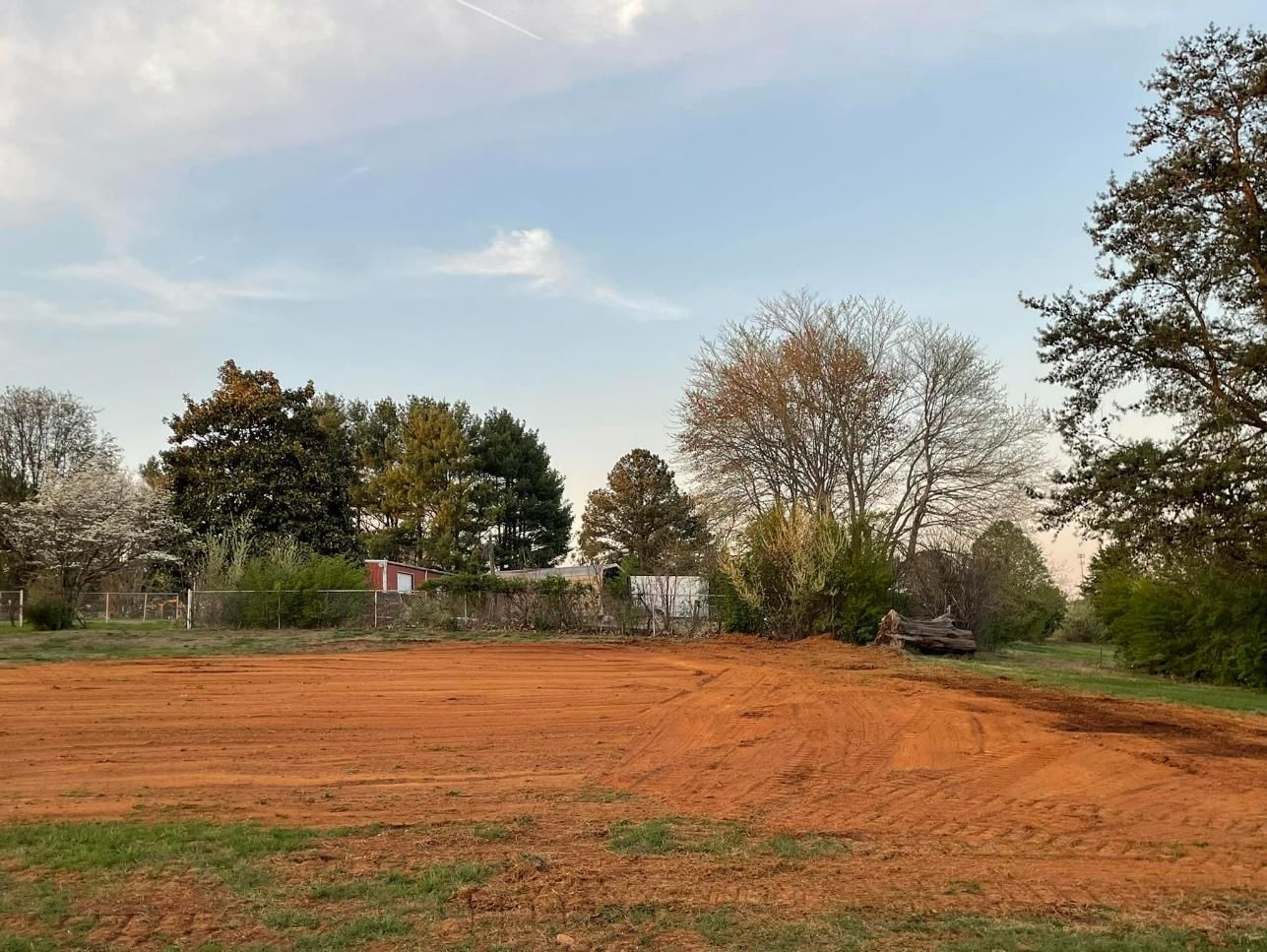 Red dirt clearing with trees under a cloudy sky.