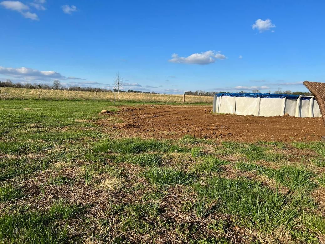 Green field with an above-ground pool, a bright blue sky with a few clouds.