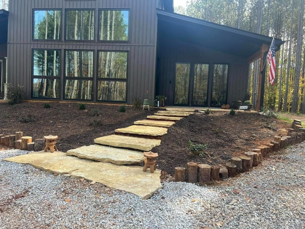 Stone steps leading to a dark brown house with large windows. Landscaping with mulch and wood edging.