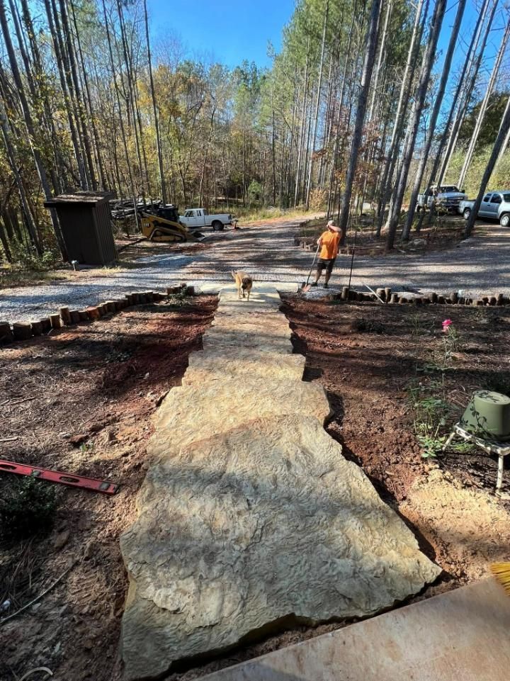 A rock path is being built through a dirt area. A person and a dog are in the distance.