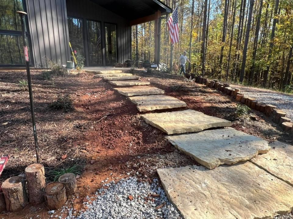 Stone pathway leading to a cabin entrance, surrounded by red dirt and trees.