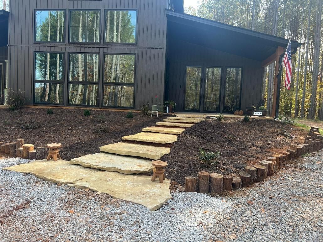 Brown house with a stone pathway, surrounded by landscaping and gravel.
